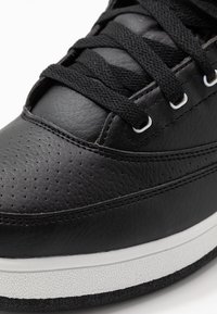 Avant de basket en cuir noir avec perforations, lacets noirs passés dans des œillets blancs et une semelle intermédiaire blanche texturée.