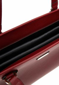 Sac à main texturé rouge avec une fermeture éclair, doté d'un intérieur en tissu noir et de trois compartiments. Comprend un détail métallique.