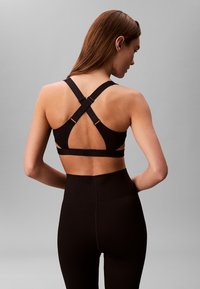 Sujeción deportiva negra con un diseño de espalda en X que cuenta con tirantes ajustables, detalles recortados y una textura suave. Combinada con leggings negros de cintura alta.
