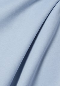 Tessuto di cotone azzurro chiaro con una superficie liscia, caratterizzato da una leggera elasticità e una tessitura semplice, che mostra pieghe e riprese alla luce naturale.
