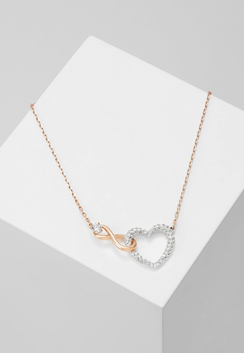 Collier en chaîne en or rose avec un symbole infini et un pendentif en forme de cœur incrusté de petits pierres précieuses claires.
