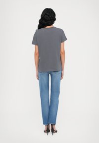 Grijze, kortekout T-shirt in combinatie met lichtblauwe, rechte jeans. Het model draagt zwarte hoge sandalen. Eenvoudig ontwerp, strakke lijnen.