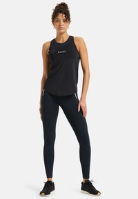 Black athletic tank top with Roxy logo, paired with form-fitting black leggings featuring side zippers. Model is in a neutral pose.
