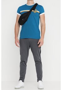 Camisa corta de manga azul con ribete blanco y rayas horizontales, combinada con pantalones grises ajustados y un bolso cruzado negro. Zapatillas blancas.
