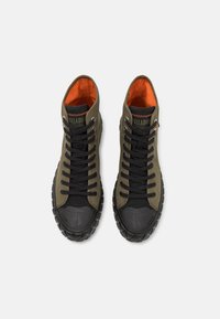 Sneakers de tip high-top, cu pânză de culoare verde măsliniu, șireturi negre, capac din cauciuc pe vârf, talpă texturată neagră și căptușeală interioară portocalie.