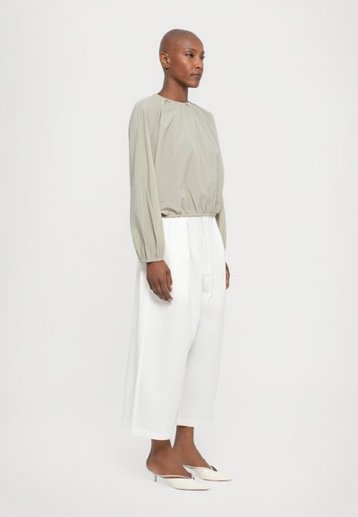 Top grigio chiaro a maniche lunghe con polsini arricciati, abbinato a pantaloni bianchi a gamba larga. Outfit completato con mule bianche con punta a punta e tacco.