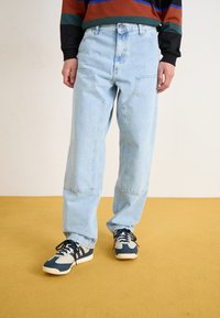 Jeans de mezclilla azul claro con un corte holgado, con bolsillos frontales en ángulo y un ligero desgaste, combinados con zapatillas navy y beige.
