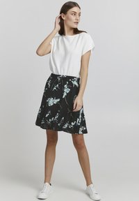 Top alb cu manșă scurtă și fustă neagră cu model floral albastru. Fusta are o dantelă la margine și o talie elastică, asortată cu pantofi sport albi.
