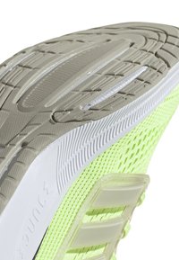 Leichter Laufschuh mit einem hellen neongrünen Mesh-Obermaterial, einer strukturierten beigefarbenen Gummisohle und weißen Akzenten entlang der Zwischensohle.