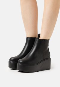 Stivali alla caviglia neri realizzati in pelle liscia, con un design elegante, punta rotonda e una spessa suola piattaforma.