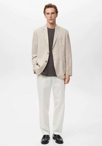 Blazer de lino beige con dos botones, camiseta gris debajo, pantalones blancos, zapatos negros. Diseño simple con corte a medida. Sin patrones ni acentos.