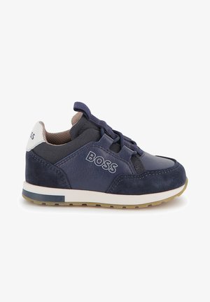 Marineblaue Sneakers aus einer Mischung aus strukturiertem Wildleder und glattem Leder, mit weißem Branding und einer kontrastierenden beigen Sohle.