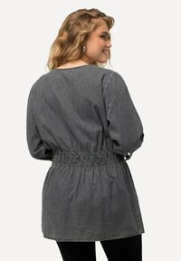 Tunika in denim grigio con una vestibilità rilassata, vita arricciata, maniche lunghe e scollatura rotonda. Texture morbida con leggere variazioni.