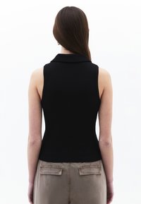 Haut sans manches noir avec un col et une coupe ajustée, associé à un pantalon beige avec poches arrière. Texture lisse.