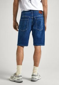 Pantalones cortos de mezclilla en un lavado azul oscuro, con un diseño clásico de cinco bolsillos, costuras visibles y un parche de cuero en la parte trasera de la cintura.
