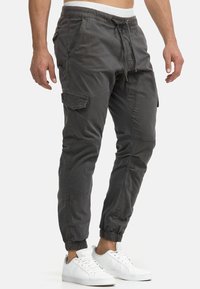 Graue Cargo-Hosen mit einem Kordelzugbund, schmal zulaufenden Beinen und elastischen Bündchen. Sie verfügen über mehrere Utility-Taschen und eine glatte Baumwolltextur.
