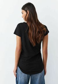 Must musta lühikeste varrukatega särk ümarate äärtega, pehme materjaliga, nähtav tagantpoolt, koos lahtiste siniste teksadega.