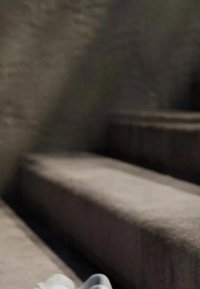 Svijetlosivi stepenici prekriveni tkaninom s teksturiranom površinom, koji vode nagore. Bijela tenisica s zelenim akcentima djelomično je vidljiva na donjem stepeniku.