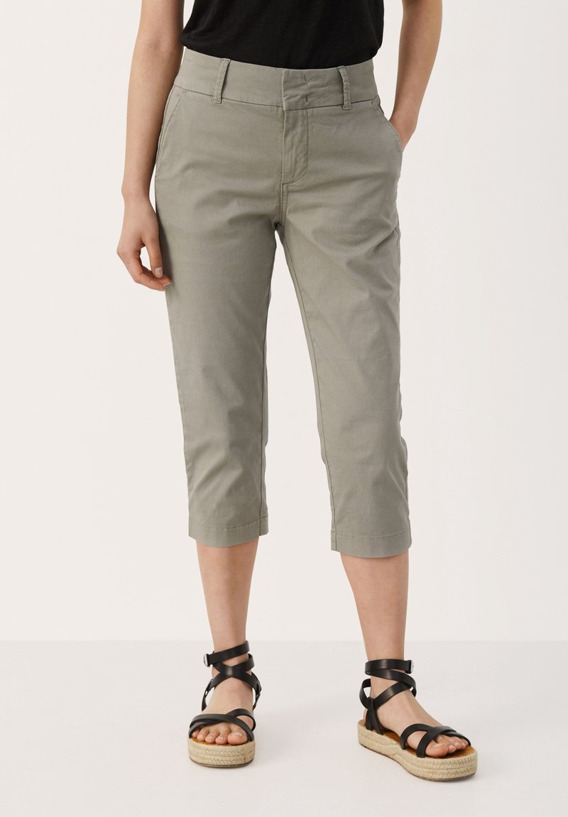 Světlé šedé cropped kalhoty s hladkým povrchem, předními kapsami a dobře padnoucím pasem, ve spojení s černými sandály na řemínky.