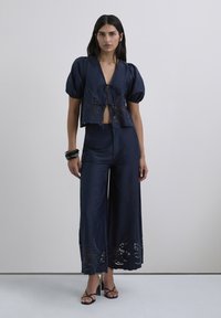 Conjunto de dos piezas en azul marino que incluye una blusa corta con mangas abullonadas y detalles de encaje, combinada con pantalones de pierna ancha, ambos en suave tela de satén.