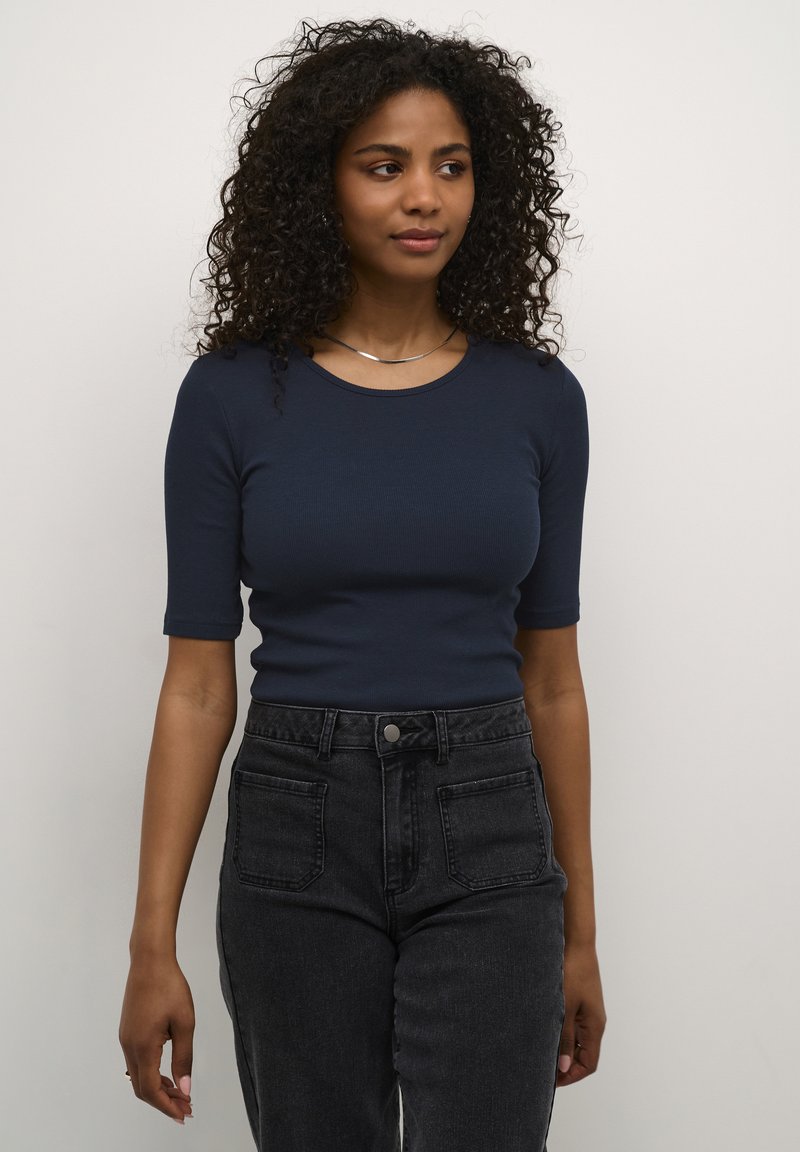 Haut à manches courtes côtelé bleu marine associé à un jean noir taille haute avec poches avant et fermeture à bouton. Simple collier en chaîne argentée.