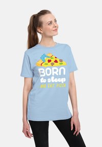 Světle modré bavlněné tričko s grafikou pizzy a medvěda, s textem "NAROZENÝ k spánku A JÍDLO PIZZY" v bílé a žluté barvě.