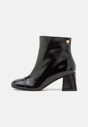 Sort patenteret læder ankelstøvle med firkantet tå, kraftig hæl og en guldfarvet hjerteaccent på ydersiden. Glat, blank finish.