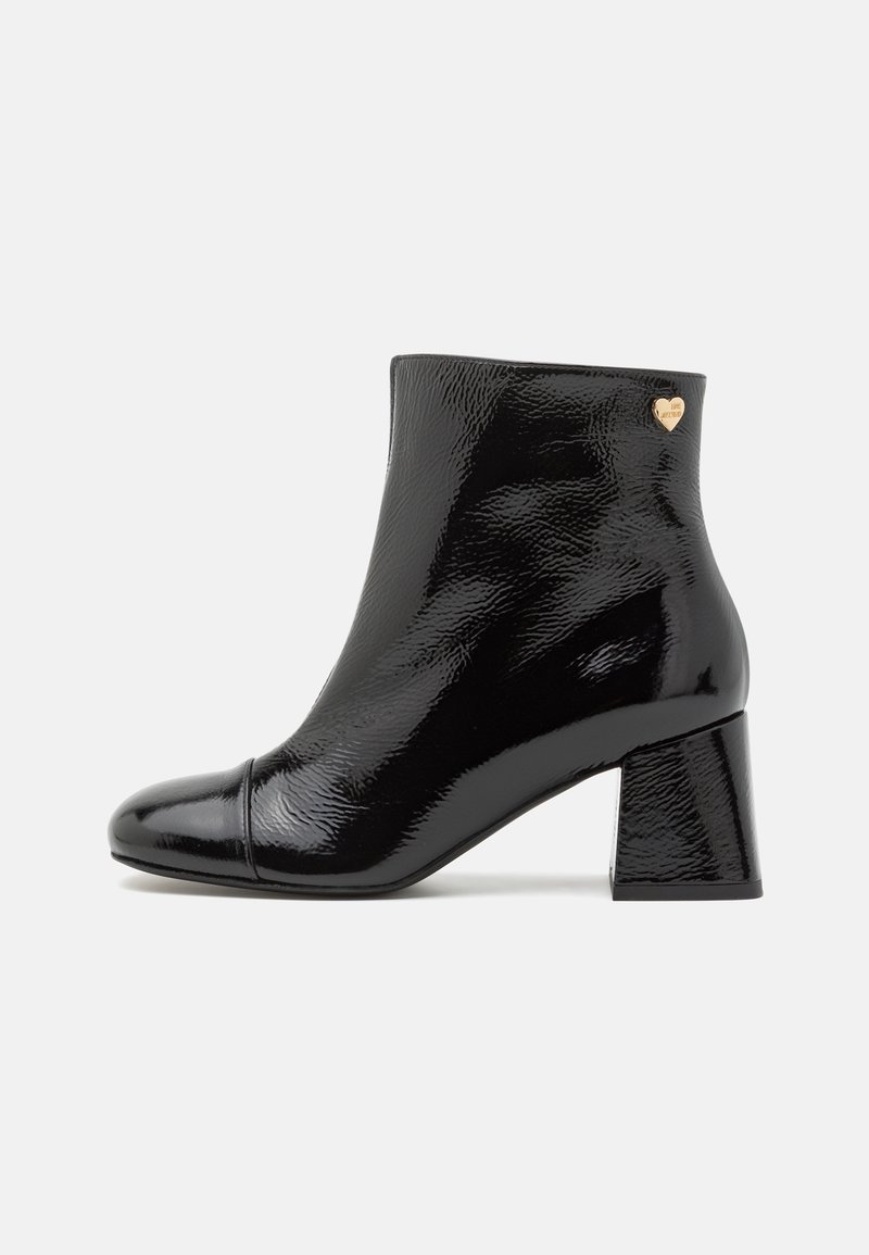 Melnas lakota ādas potītes zābaki ar kvadrātu purngaliem, masīvu papēdi un zelta sirds akcentu ārējā pusē. Gluda, spīdīga virsma.