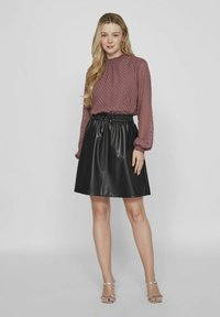 Vaaleanpunainen pitkähiha blouse, jossa on teksturoitu chevron-kuvio, yhdistettynä mustaan laskostettuun nahkahameeseen, jossa on joustava vyötärö.