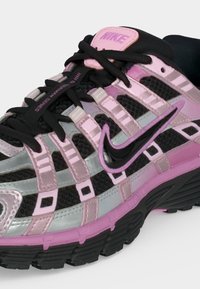 Μαύρο και ροζ παπούτσι Nike με μαύρα κορδόνια, ροζ και ασημί επενδύσεις, υφή στην σόλα και το λογότυπο Nike στο πλάι και στη γλώσσα.