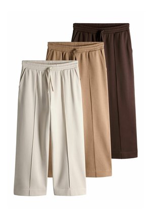 Tre par vidde bukser med elastiske taljebånd og snore, i lyse beige, tan og mørkebrun farver, arrangeret med overlap.
