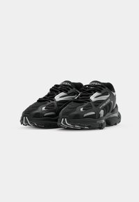 Zapatillas deportivas negras con parte superior de malla y sintético, acentuadas con detalles plateados, que cuentan con una suela acolchada y diseño de cordones.