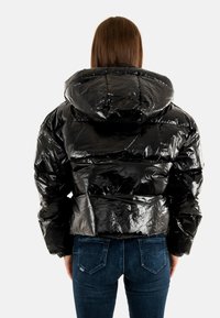 Giubbotto invernale nero con una texture lucida e arricciata, cappuccio oversize e cuciture orizzontali. Indossato con jeans blu scuro.