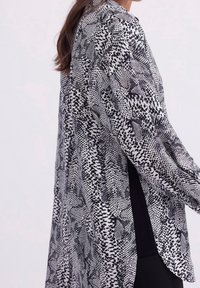 Black and white patterned blouse with long sleeves, featuring a blend of abstract shapes, textured fabric, and a loose fit for comfort.