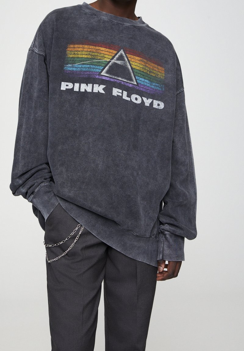 Felpa grigia oversized con scollo a girocollo, caratterizzata da un logo colorato dei Pink Floyd e un design grafico arcobaleno sulla parte anteriore.