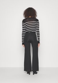 Czarna i biała bluzka z długim rękawem w paski, zestawiona z czarnymi spodniami typu flare o wysokim stanie, charakteryzującymi się gładką teksturą i dopasowanym krojem.