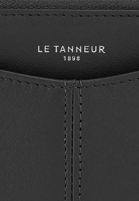 Schwarzes Lederprodukt mit glatter Textur, sichtbaren Nähten und eingeprägtem Markennamen "LE TANNEUR 1898" in weißer Schrift.