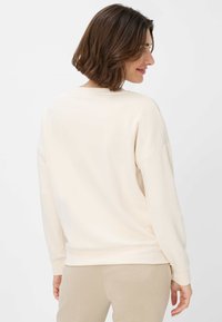 Cremefarvet sweatshirt med afslappet pasform, rund hals og ribbede manchetter. Blødt stof med en glat overflade, båret med lyse beige bukser.