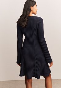 Granatowa sukienka z prążkowanego dzianiny z rozszerzanym dołem i długimi rękawami, z okrągłym dekoltem i bocznymi rozcięciami dla swobody ruchu.