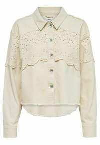 Chemisier court beige clair avec un boutonnage à l'avant, un col et de la broderie œillet festonnée sur les manches. Il présente des détails avec un ourlet effiloché.
