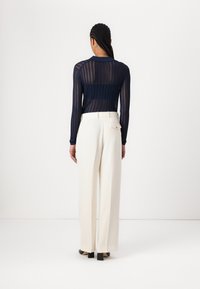 Navy ribbed knit long-sleeve top paired with high-waisted white wide-leg trousers. Black block-heeled shoes, back view.
