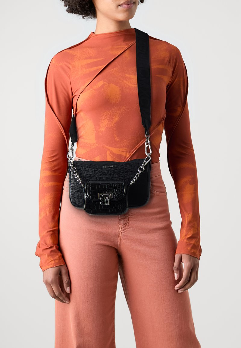 Borsa a tracolla in pelle sintetica nera con dettagli in catena argentata e una borsetta più piccola in texture; indossata con un top arancione aderente e pantaloni rosa chiaro.