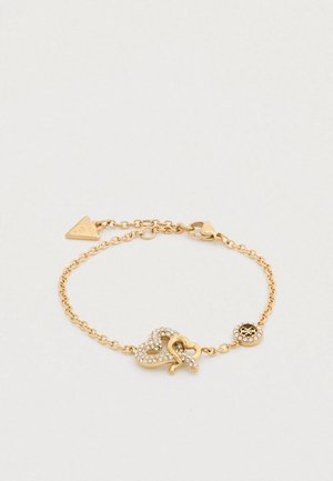 Bracelet ton or avec un design de cœur relié orné de cristaux clairs et un charme décoratif. Style chaîne avec une fermeture à clip.