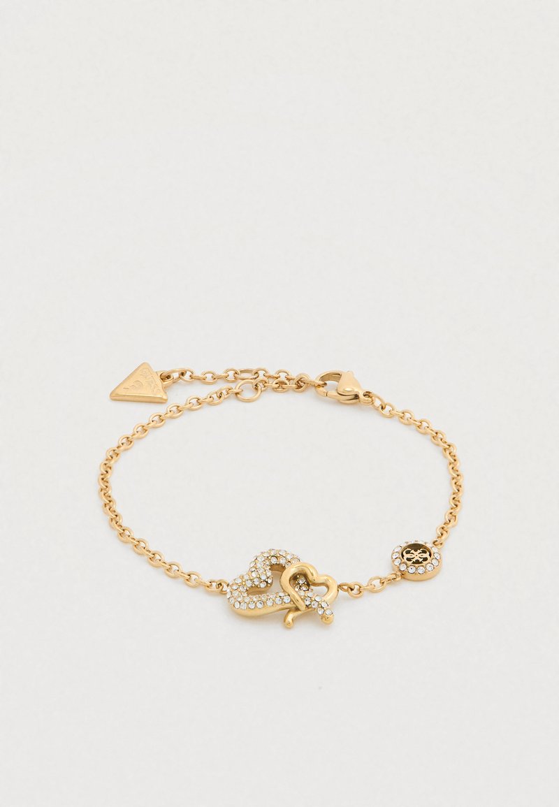 Βραχιόλι σε χρυσό τόνο με σχέδιο συνδεδεμένες καρδιές διακοσμημένο με διάφανα κρύσταλλα και διακοσμητικό γούρι. Στυλ αλυσίδας με κούμπωμα.