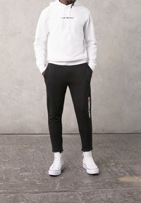 Vit huvtröja med snörning och svart logga. Svarta joggers med sidofickor och vit branding, i kombination med vita sneakers.