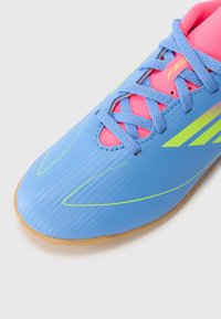 Scarpa sportiva blu realizzata in materiale sintetico, con strisce verde neon, accenti rosa, superficie testurizzata e suola in gomma.