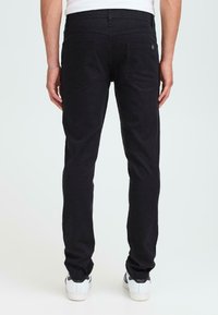 Sorte denimjeans med slank passform, med to baklommer, diskrete sømdetaljer og middels livhøyde, kombinert med hvite sneakers.