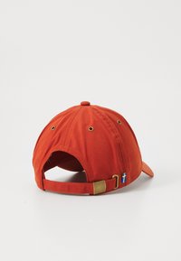 Rustfarvet baseballcap med justerbar rem og messingspænde, lille svensk flagtags i nærheden af bagåbningen, på hvid baggrund.