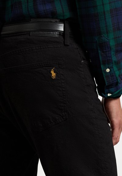 Black jeans with a back pocket featuring a small, embroidered gold polo player logo. Accompanied by a green and blue plaid shirt.
