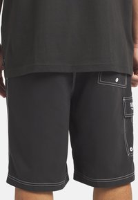 Mustat cargo-shorts, joissa on valkoiset ompeleet, sivutaskut ja napilla suljettavat läpät. Materiaali vaikuttaa kevyeltä ja kestävältä.